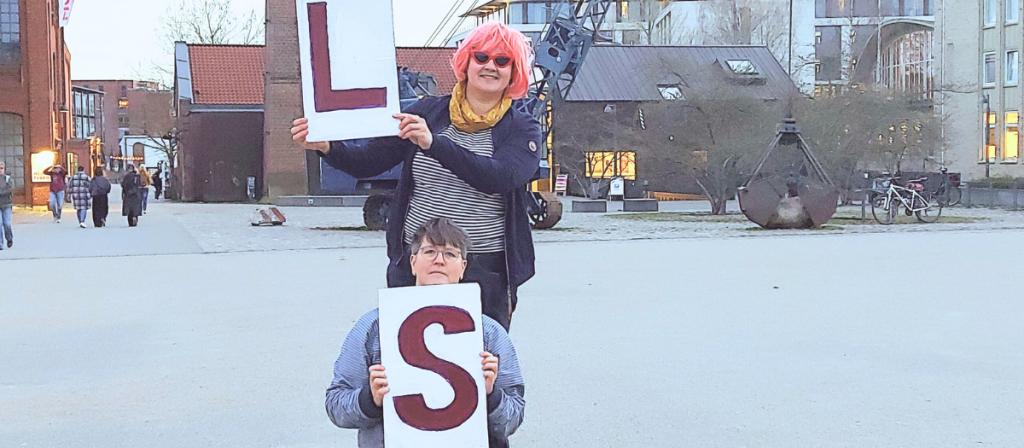 2 Personen halten Schilder mit Buchstaben hoch.
